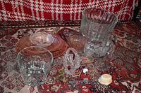 Photo of mixed glassware on patterned cloth including clear and pink Depression glass, crystal, cut glass, and small decorative items.