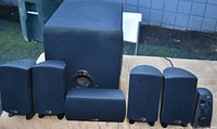 Full view of 5 satellite speakers and 1 large subwoofer on table outdoors
