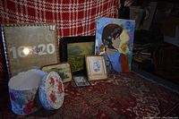 Lot arranged on a patterned carpet with red and white woven fabric backdrop, showing framed paintings and decorative boxes as lot contents.
