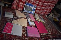 Photo showing ten photo albums of various sizes and colors arranged on a patterned blanket with a box labeled 'Happy Moments' containing loose photographs.