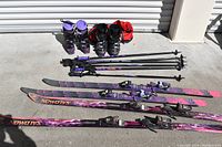 View of both complete ski sets with boots, skis, poles, and red ski bag, outdoors in front of a metal shutter