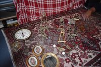 Photo showing multiple small vintage picture easels, two round framed floral pictures, a gold-toned mirror, an oval vintage clock, and other decorative items arranged on a patterned rug.