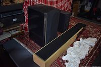 Three black speakers and two white carved ornamental wall decor pieces on a patterned rug.