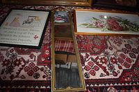 Photo showing vertical mirror with two framed pictures placed on a patterned red carpet.