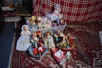 Wide view of the vintage dolls collection showing various dolls in a plastic tub, baskets, and plates on a patterned red rug