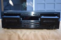 Front view of Yamaha cassette deck showing dual cassette compartments with doors open, multiple control buttons, and headphone jack.