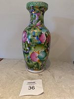 Front view of colorful vintage Asian porcelain vase with floral and grape designs, green neck rim.