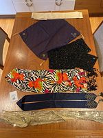 Photo showing all six scarf accessories laid out on a wooden table, including floral zebra print scarf, navy blue scarf with gold embroidery, sequined scarves, and cream sash.