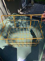 Yellow metal wire basket with grid pattern shown from top angle on green surface outdoors.