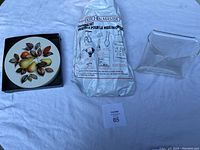 Photo showing the six trivets with fruit artwork, the sealed Kitchen Master canning set plastic bag, and the clear Lucite napkin holder on a white background.