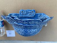 Front view of blue ceramic wall planter showing detailed paisley and floral patterns with scalloped top edge and built-in hanger.