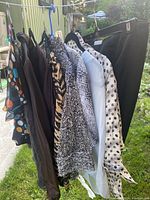 Image showing multiple women's tops and a black skirt hanging on hangers outdoors, variety of colors and patterns visible.