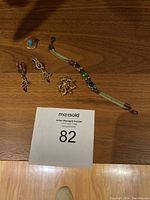 Photo showing all jewellery items on wooden surface including earrings, ring, brooch, and bracelet with seller auction number card
