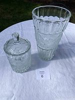 Photo showing the crystal vase and covered dish on a white tablecloth, clear glass with rose pattern visible, vase taller and wider at top, covered dish with lid beside it.