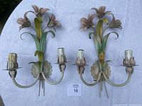 Photo showing both French antique metal wall sconces with floral designs and three candle holders each on a white cloth background.