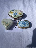Top view of three Limoges porcelain pill boxes, heart-shaped, scalloped rectangular, and oval, showing floral hand-painted designs