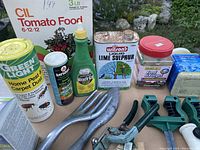 Photo showing gardening chemicals including CIL Tomato Food, Green Light Pest Dust, Miracle-Gro, Wilson Liquid Lime Sulphur, Diazinon insecticide, Keri dust killer. Also includes gardening hand tools like trowels, cultivator, pruning shears, hose line holders.