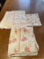 Five linens arranged including euro shams, pillowcases, and sheet showing floral patterns and lace details