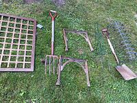 Metal garden items laid on grass including table parts with cast iron legs, pitch fork, bench frame, trellis, shovel, and window box frame shown from above.