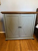 Front view of distressed teal cabinet with natural wood top and two doors with diamond panel design and round knobs.
