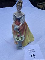 Front view of Royal Doulton Alexandra figurine watering flowers on pedestal with flowers.