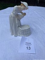 Side view of the Royal Doulton Mother and Baby figurine on a white cloth background, showing the mother leaning over the bassinet holding the infant.