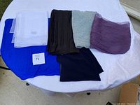 Photo showing six scarves laid out on a table: a sheer white scarf, bright blue scarf, sheer black scarf, knitted mint green scarf, crinkled purple scarf, and a smooth black scarf.