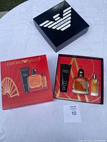 Photo showing the gift set inside the open black box with Emporio Armani logo, featuring perfume bottles and shampoo tube along with the outer red packaging.