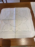 Close view of one pillow case showing heart-shaped blue floral embroidery on white fabric with scalloped edges, laid flat on wooden table