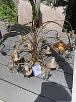 Full top view of the vintage chandelier on an outdoor table showing the gold-tone metal arms and clear crystal flower accents surrounding the bulb holders.
