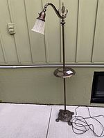 Full view of vintage floor lamp with curved brass-toned stand, white glass shade, and attached ornate metal table tray; black cord visible