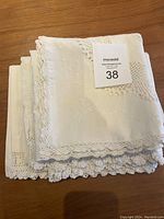 Stacked white linens consisting of a square cloth with crocheted lace edges visible on top.