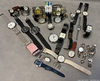 Full view of 32 assorted dress watches on a gray surface showing different dial designs and strap materials