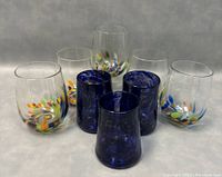 Front view showing 5 colorful stemless wine glasses behind 3 cobalt blue glasses arranged in front, displaying vibrant colors and glass texture.