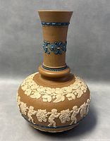 Front and side view showing the vase's bulbous body decorated with white cherubs and grapevine reliefs, blue bands on the neck, and leaf garland at the shoulder.