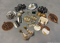 Photo showing full view of assorted jewelry including brooches, earrings, ring and hairclip on gray background