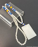 Full view of the jade beaded necklace with rectangular pendant laid out on black and gray surfaces showing the pendant and bead color details.