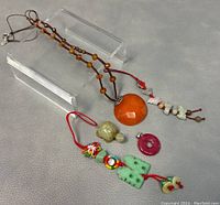 Orange faceted stone pendant necklace and multiple small pendants laid out on gray surface