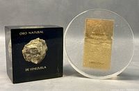 Frontal view of the natural gold rock sample encased in black block next to circular clear block with embedded gold leaf.