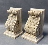 Pair of off-white Hydrostone Greek style bookends showing frontal angle with detailed acanthus leaf and scroll design.