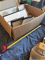 Box filled with a variety of picture frames in assorted materials and finishes, showing different sizes and shapes packed together.