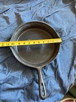 Top view of black cast iron frying pan measuring about 11 inches in diameter, showing cooking surface and handle.
