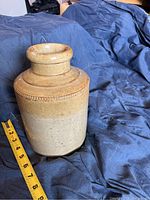 View of ceramic jar showing two-tone beige and natural clay finish with decorative beading near neck. Measuring tape indicates height of approximately 7.5 inches.