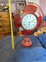 Front view of the clock showing fan blades design and Roman numeral face with measuring tape for size reference.