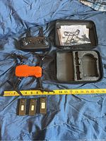 Drone, remote, 3 batteries, carrying case with spare parts, laid out with measuring tape for size reference.