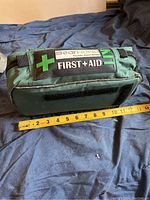 Side view of the green first aid kit pouch showing the 'Bear Toyko' label and 'First Aid' patch with a measuring tape showing about 9 inches length.