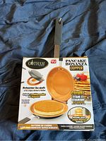 Photo showing new, unopened Gotham Steel Pancake Bonanza Copper frying pan in original packaging with details of product features in French.