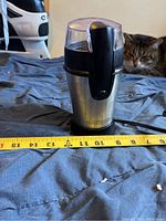 Front view of the grinder placed on a fabric surface with a measuring tape showing height approximately 7 inches.