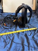 Sony black cordless over-ear headphones on a headphone stand with attached RCA cables. Measuring tape beside item.