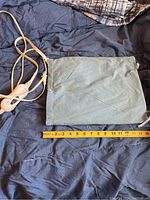 Rectangular grey fabric heating pad placed on a dark blue cloth surface with measuring tape indicating approx. 14 inches width. Attached wired controller with two buttons shown.